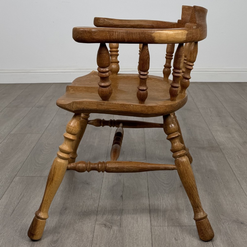 A solid oak smokers bow armchair featuring a shaped saddle seat, turned spindles, curved handrests, and splayed legs. View II