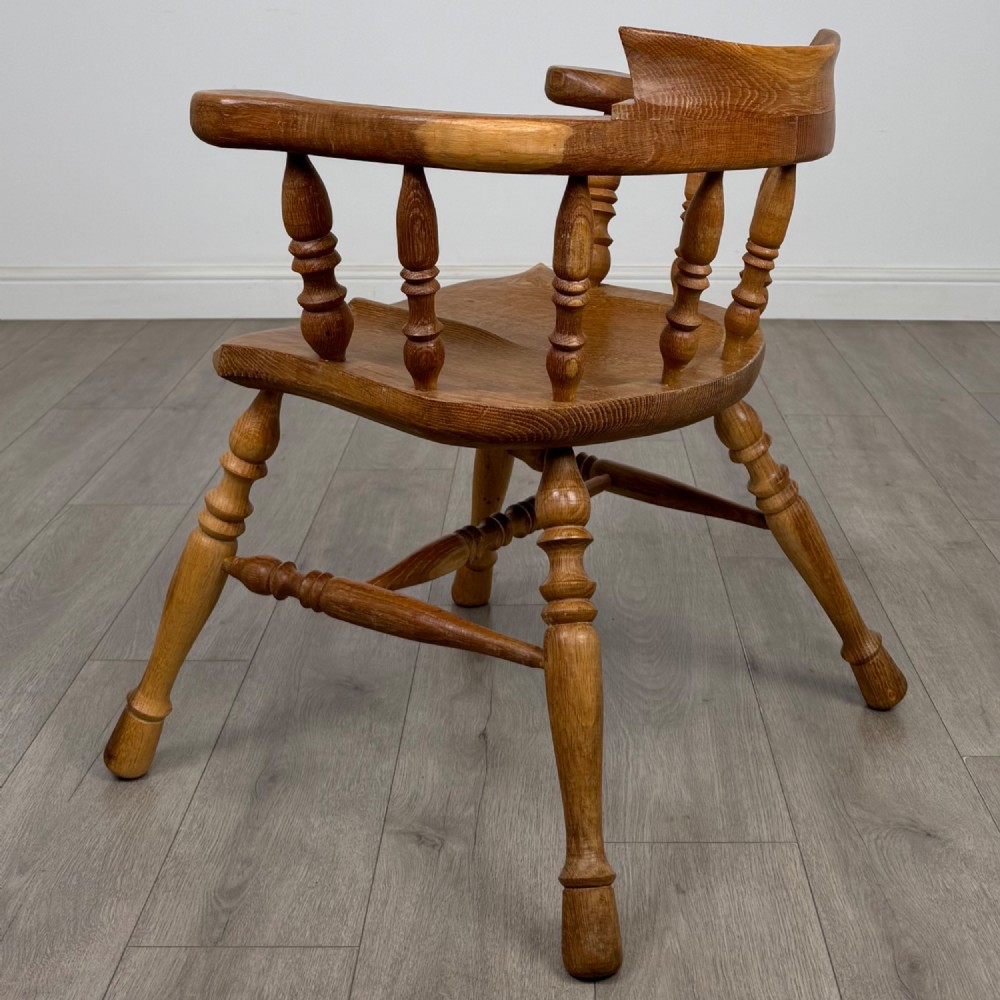 A solid oak smokers bow armchair featuring a shaped saddle seat, turned spindles, curved handrests, and splayed legs. View III
