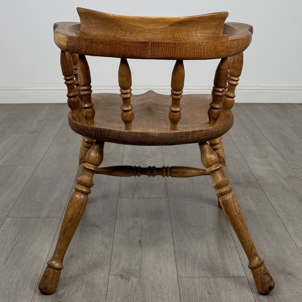 A solid oak smokers bow armchair featuring a shaped saddle seat, turned spindles, curved handrests, and splayed legs. View IV