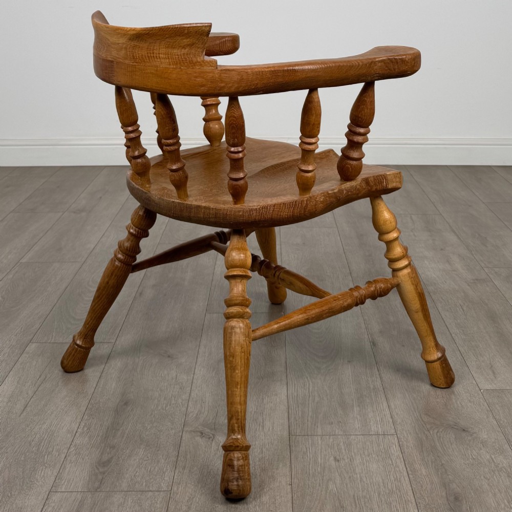 A solid oak smokers bow armchair featuring a shaped saddle seat, turned spindles, curved handrests, and splayed legs. View V