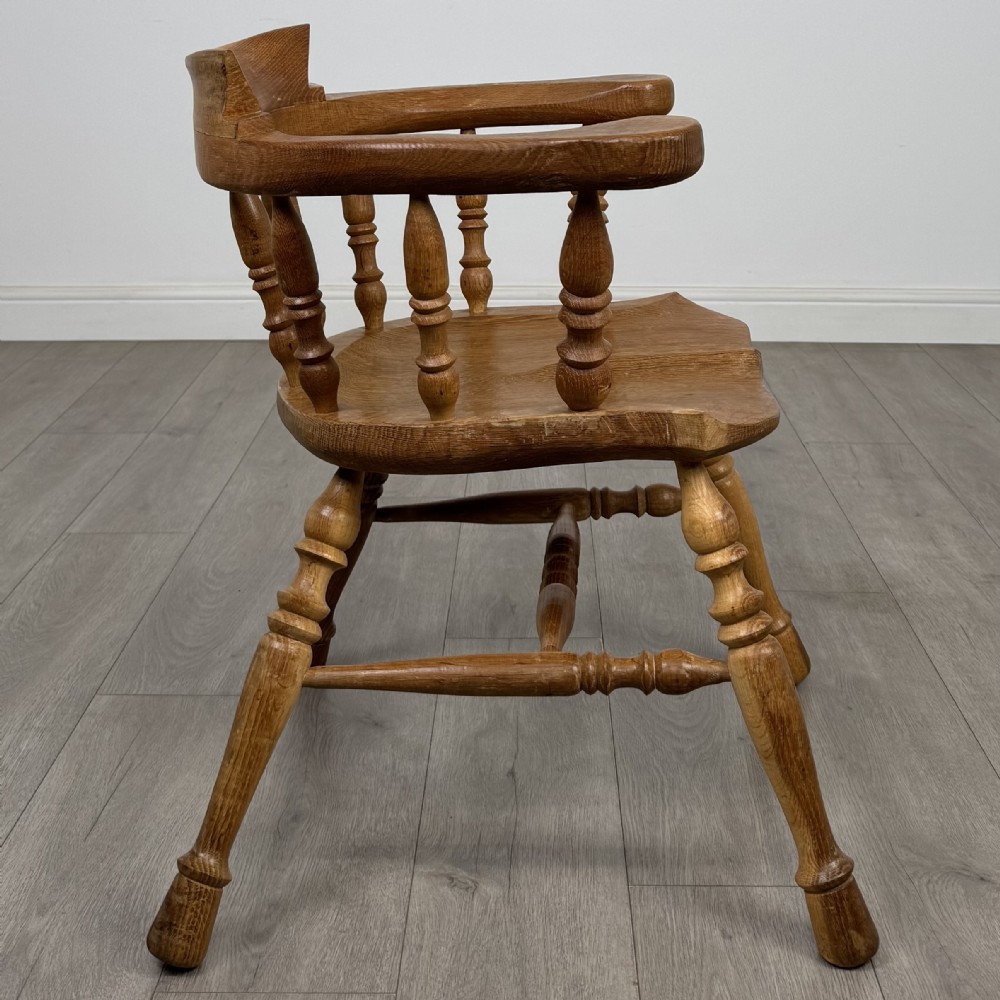 A solid oak smokers bow armchair featuring a shaped saddle seat, turned spindles, curved handrests, and splayed legs. View VI