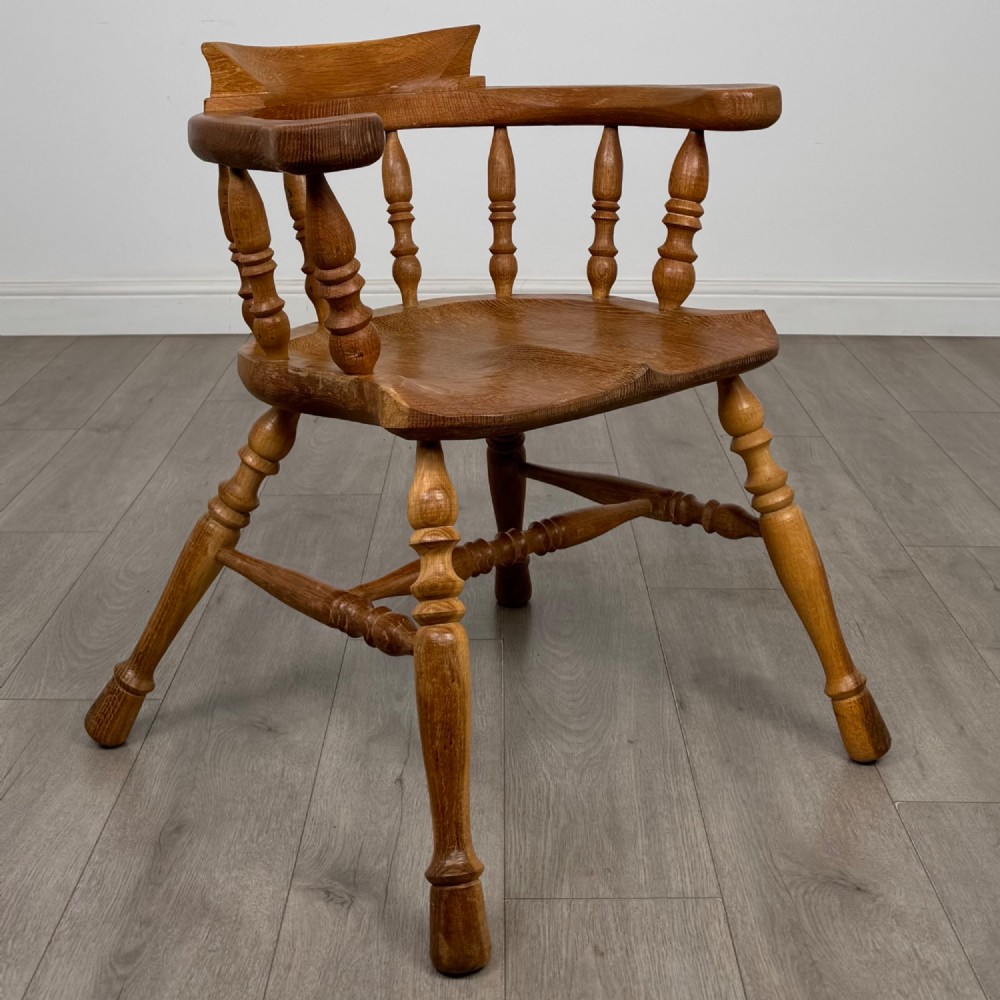 A solid oak smokers bow armchair featuring a shaped saddle seat, turned spindles, curved handrests, and splayed legs. View VII