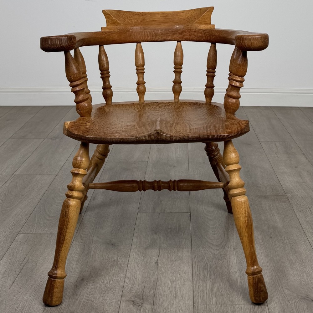 A solid oak smokers bow armchair featuring a shaped saddle seat, turned spindles, curved handrests, and splayed legs. View VIII