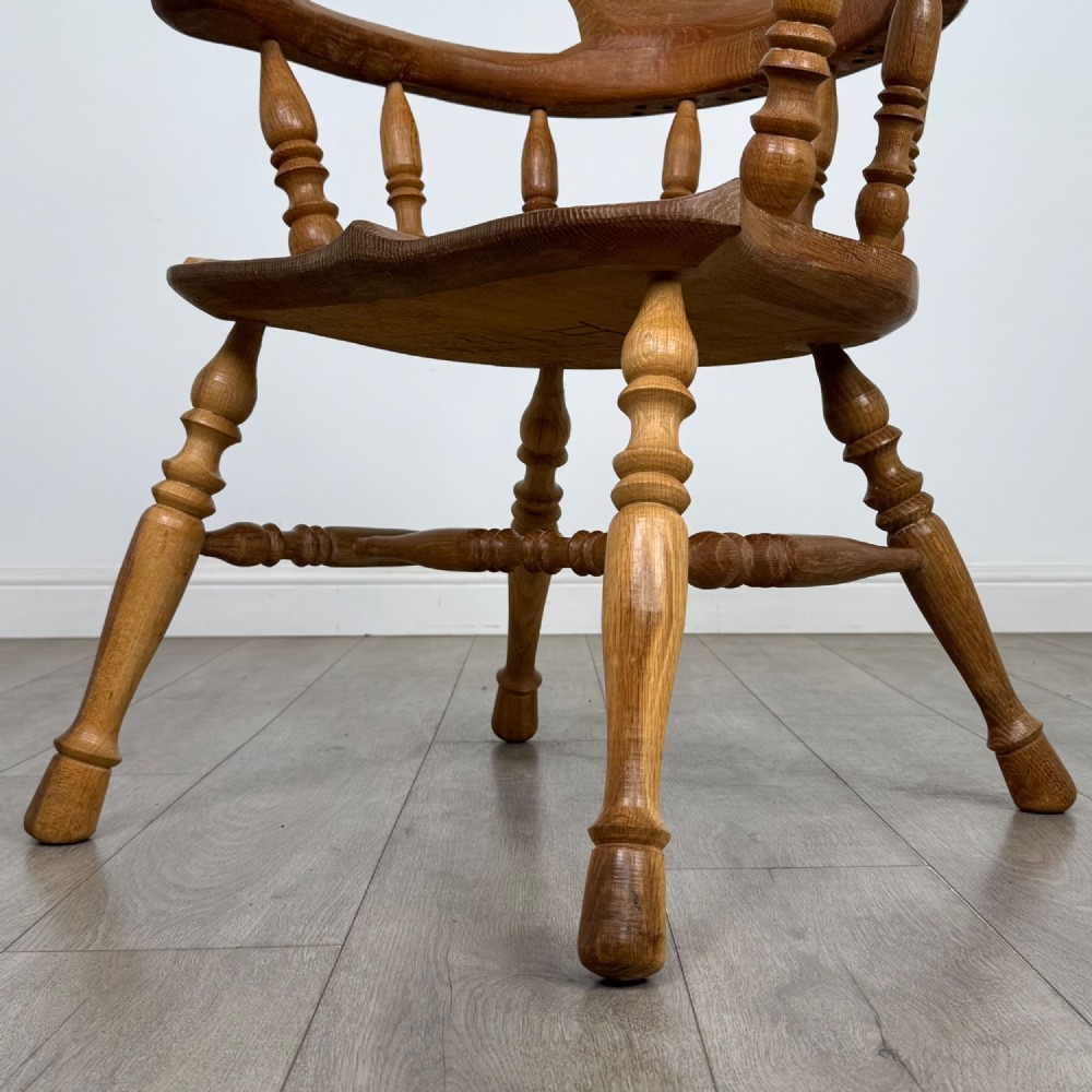 A solid oak smokers bow armchair featuring a shaped saddle seat, turned spindles, curved handrests, and splayed legs. View XI