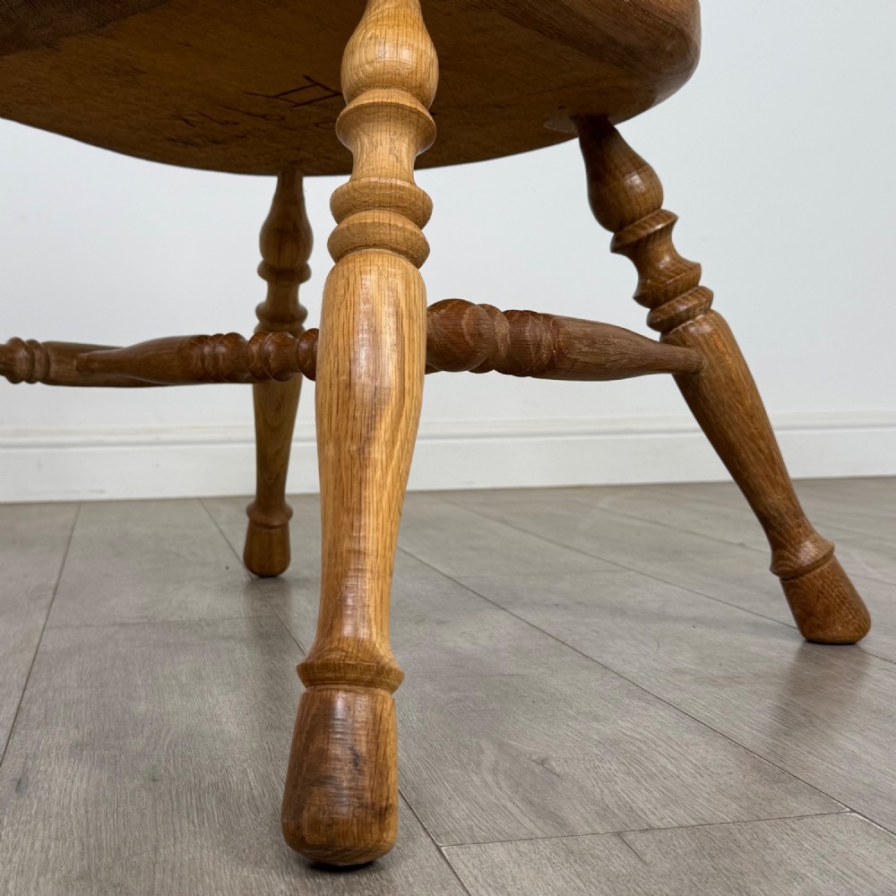 A solid oak smokers bow armchair featuring a shaped saddle seat, turned spindles, curved handrests, and splayed legs. View XII