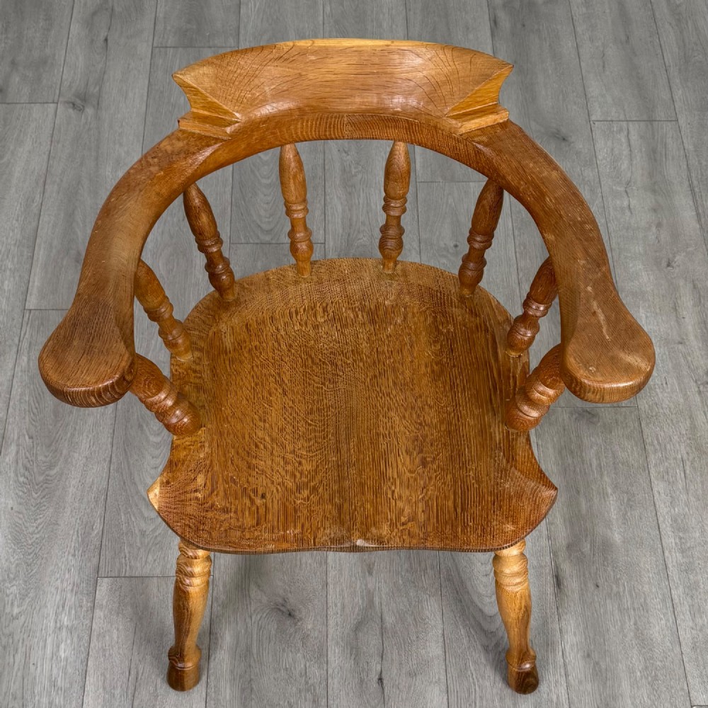 A solid oak smokers bow armchair featuring a shaped saddle seat, turned spindles, curved handrests, and splayed legs. View XIII