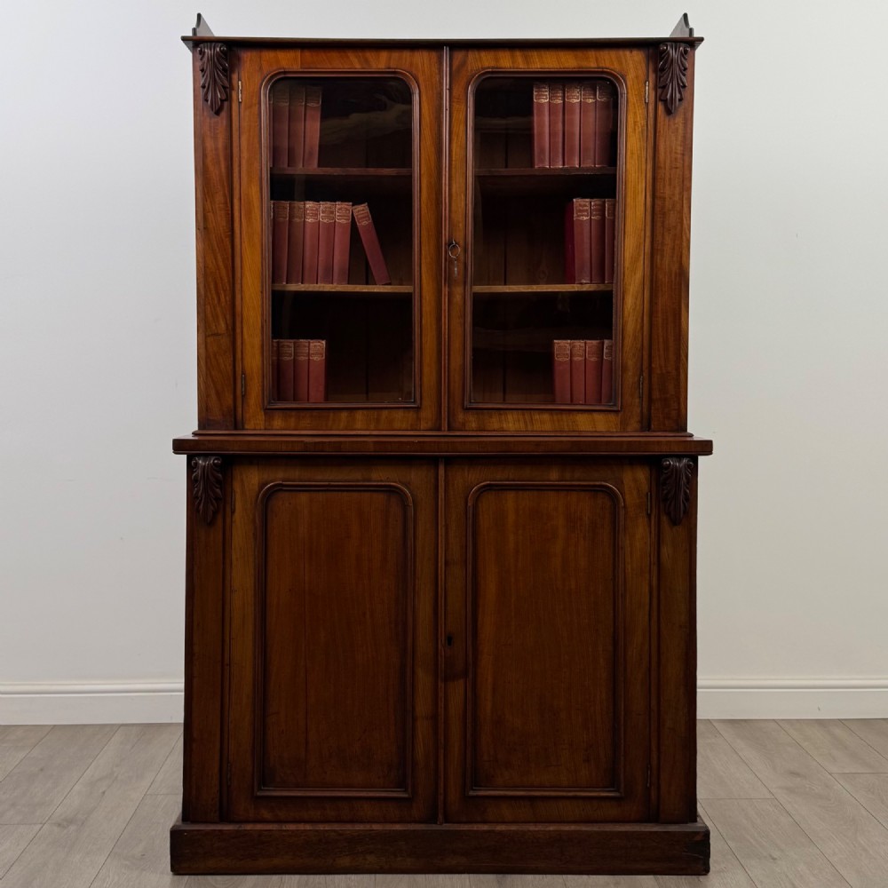 A 19th-century Victorian mahogany bookcase featuring a glazed upper display cabinet with carved corbels above a two-door solid cupboard base.