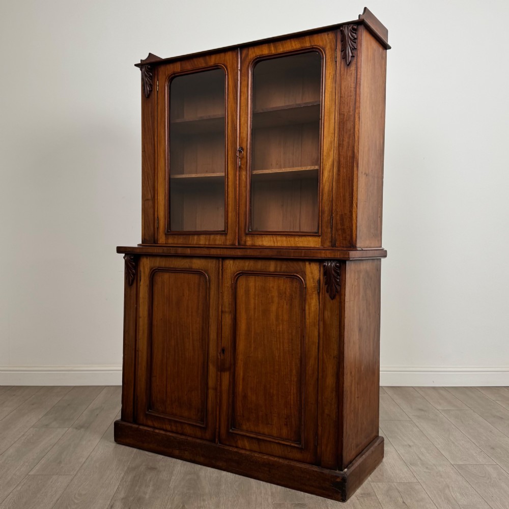 A 19th-century Victorian mahogany bookcase featuring a glazed upper display cabinet with carved corbels above a two-door solid cupboard base. View IV