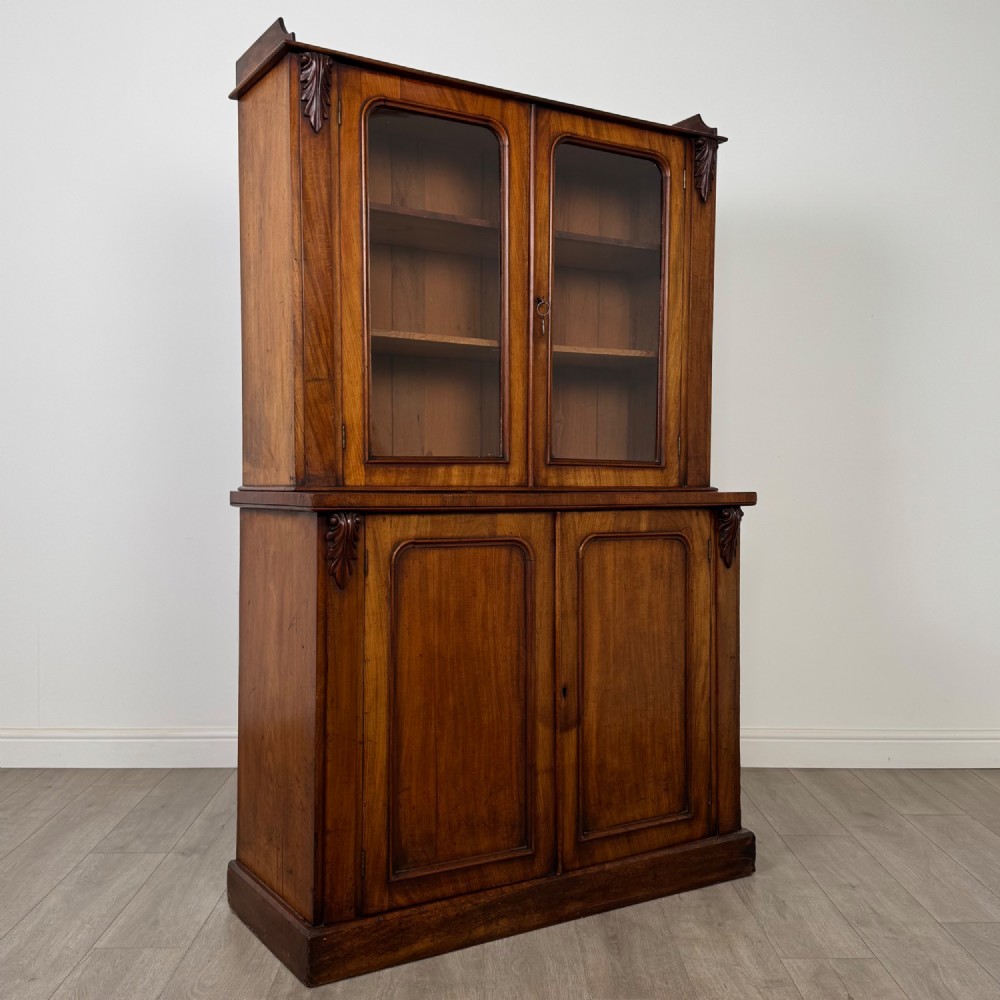 A 19th-century Victorian mahogany bookcase featuring a glazed upper display cabinet with carved corbels above a two-door solid cupboard base. View X