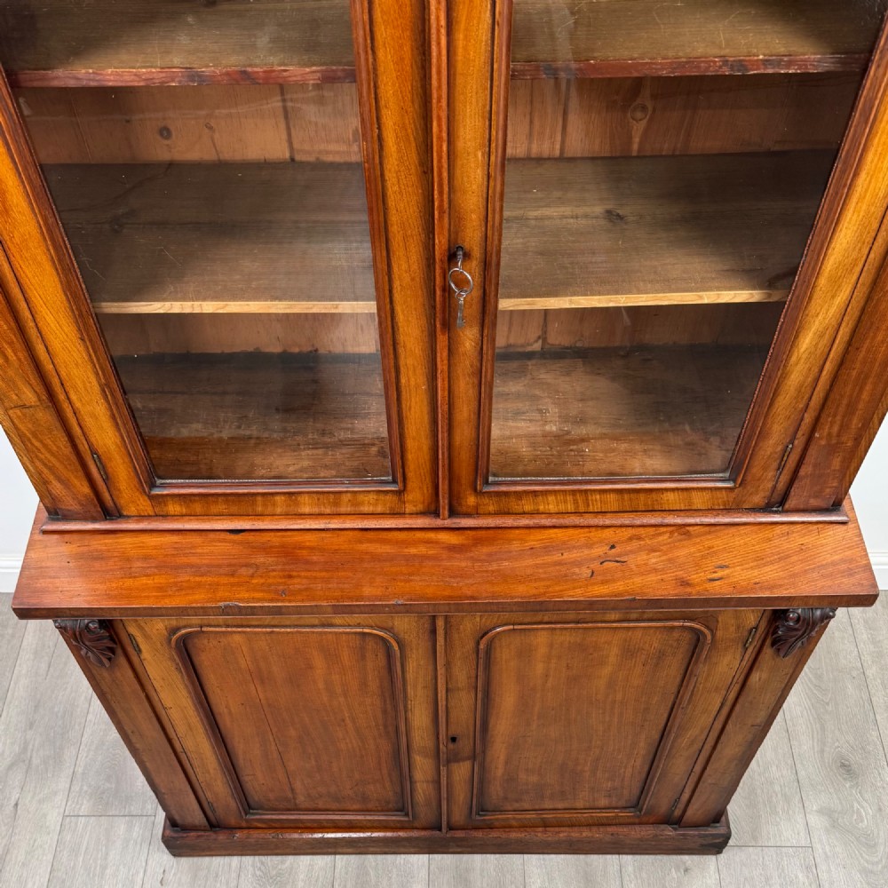 A 19th-century Victorian mahogany bookcase featuring a glazed upper display cabinet with carved corbels above a two-door solid cupboard base. View XI