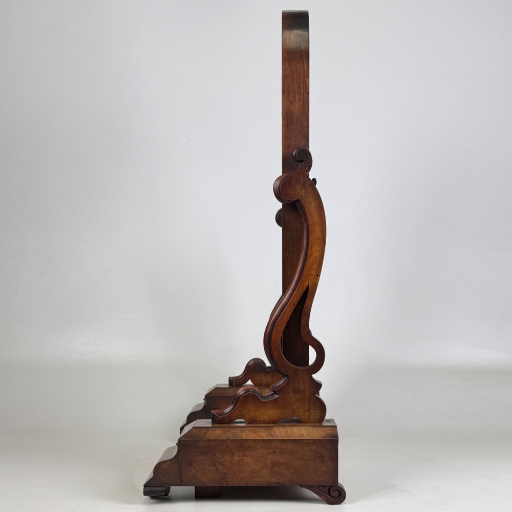 An antique Victorian dark mahogany tabletop dressing mirror featuring an arched frame supported by carved scroll uprights on a plinth base. View IV