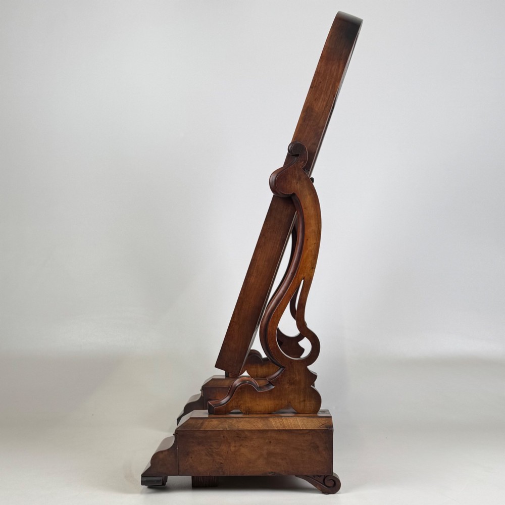 An antique Victorian dark mahogany tabletop dressing mirror featuring an arched frame supported by carved scroll uprights on a plinth base. View V