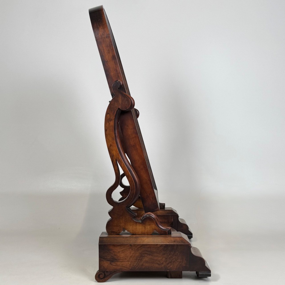 An antique Victorian dark mahogany tabletop dressing mirror featuring an arched frame supported by carved scroll uprights on a plinth base. View X