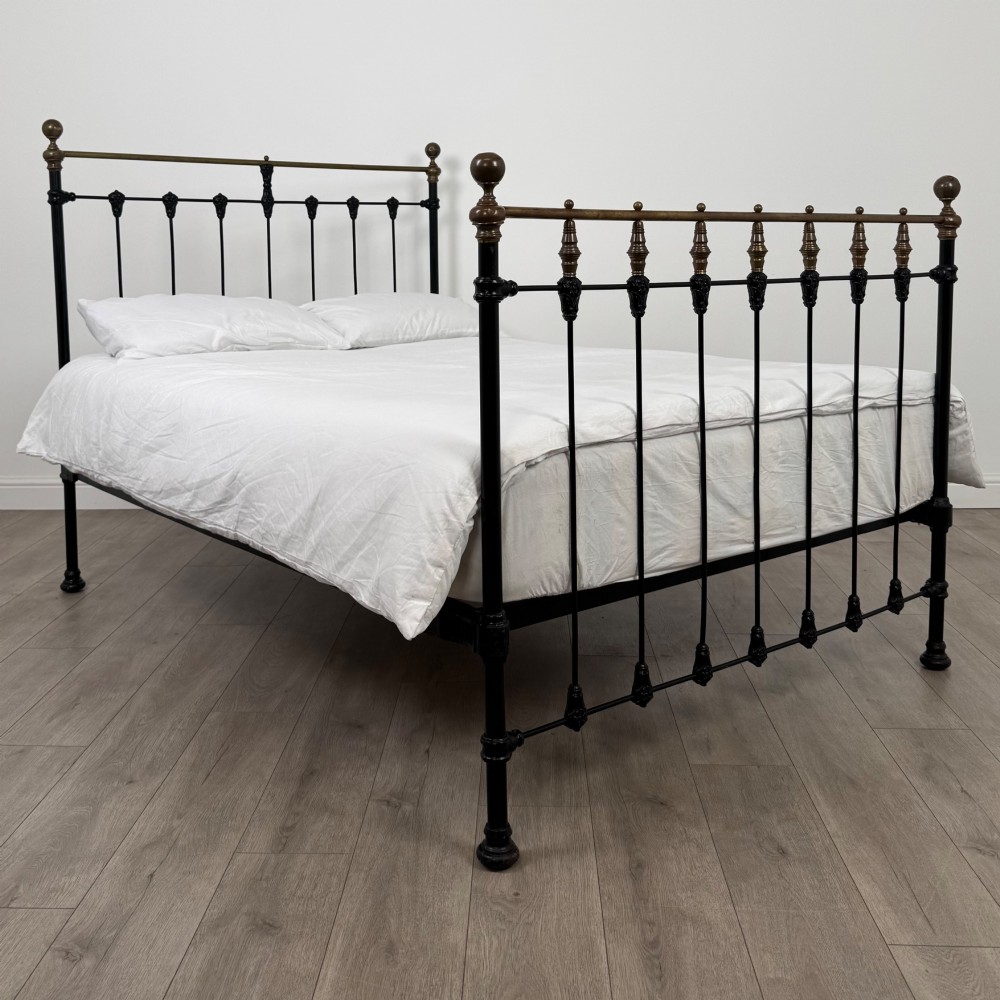 A 19th-century double bedstead featuring a black iron spindle frame with polished brass top rails and finials.