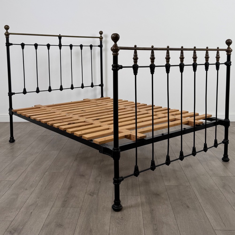 A 19th-century double bedstead featuring a black iron spindle frame with polished brass top rails and finials. View II