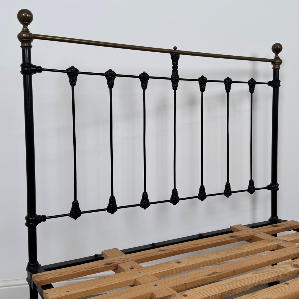 A 19th-century double bedstead featuring a black iron spindle frame with polished brass top rails and finials. View V