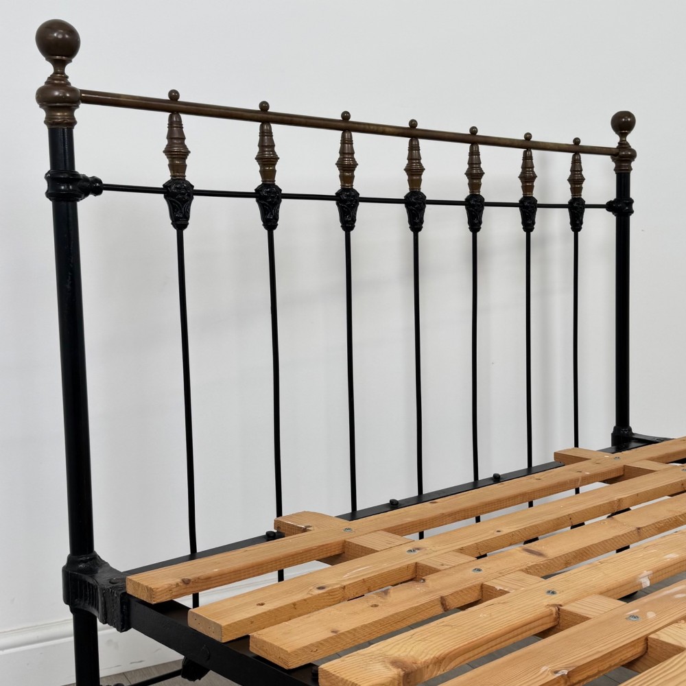 A 19th-century double bedstead featuring a black iron spindle frame with polished brass top rails and finials. View VI