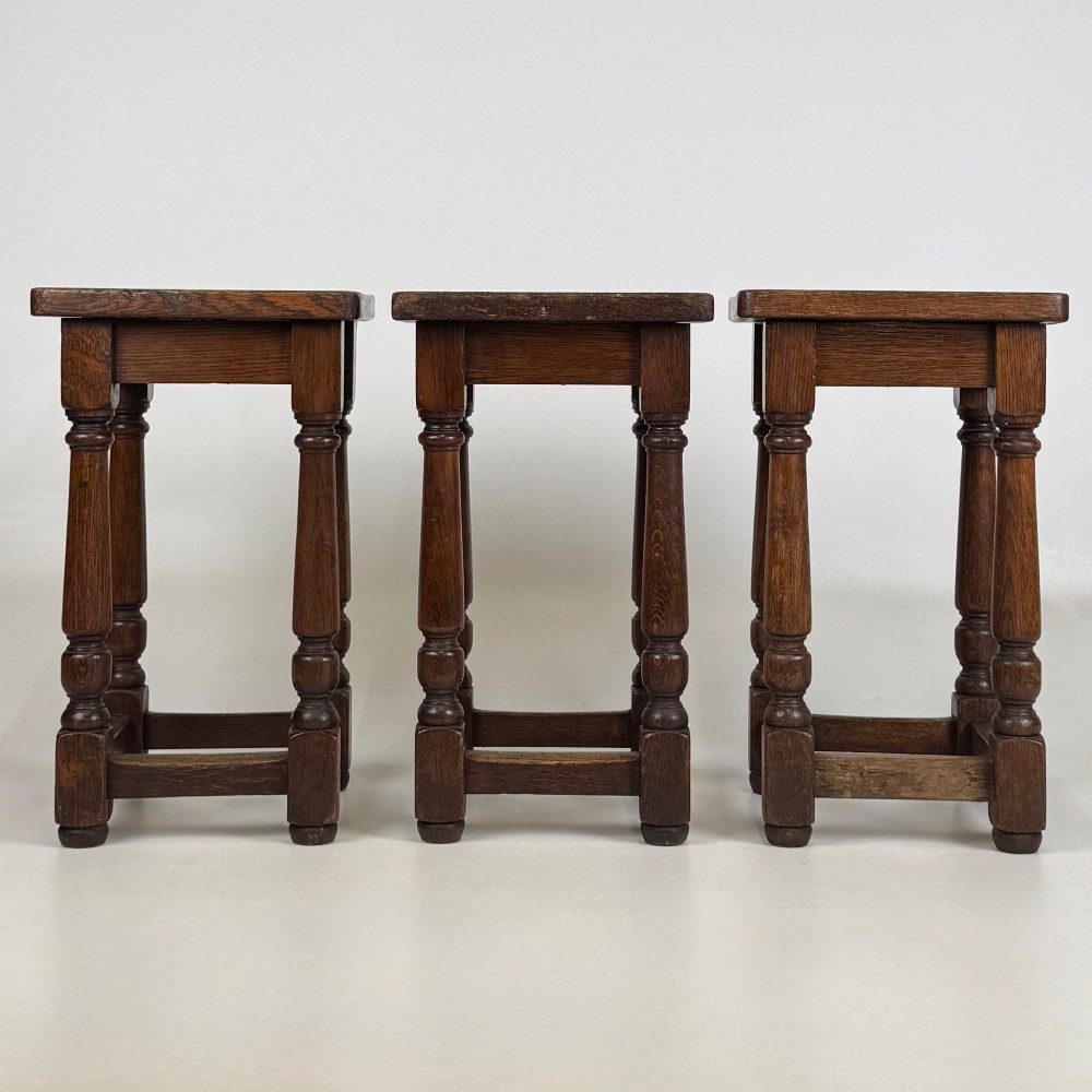 A set of three dark oak Edwardian stools featuring rectangular wooden tops, turned legs, and lower perimeter stretchers.