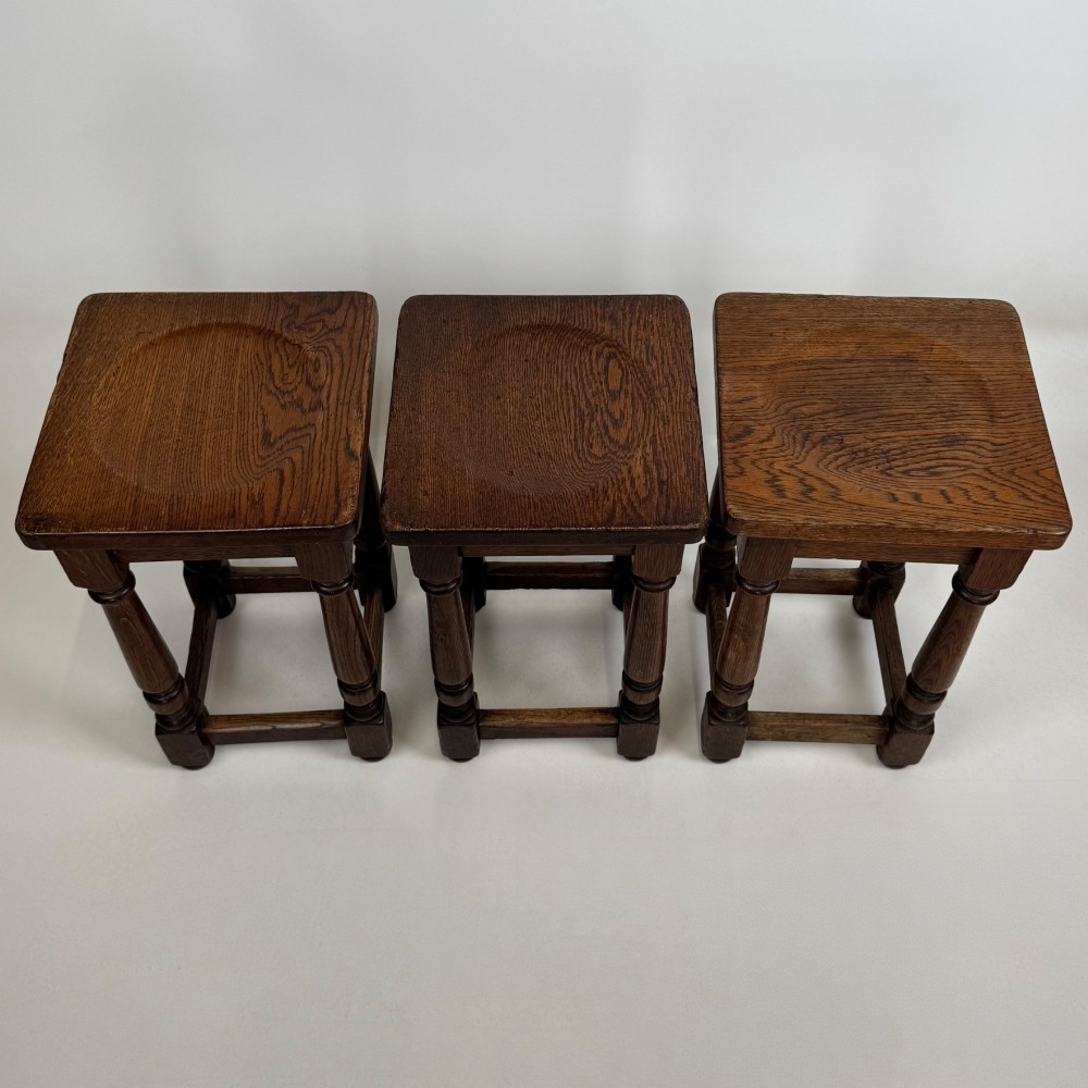 A set of three dark oak Edwardian stools featuring rectangular wooden tops, turned legs, and lower perimeter stretchers. View X
