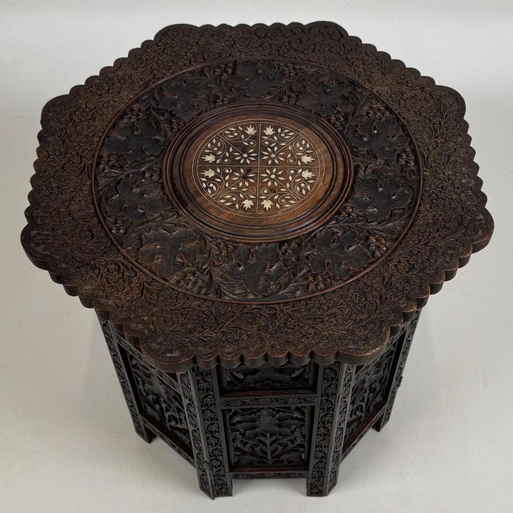 A dark brown octagonal wooden side table featuring intricate hand-carved foliate openwork panels across every side. View VI