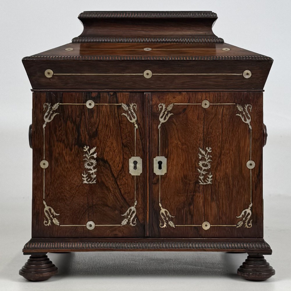 An antique dark rosewood box featuring mother-of-pearl floral inlays, twin front doors, a sarcophagus top, and turned feet.