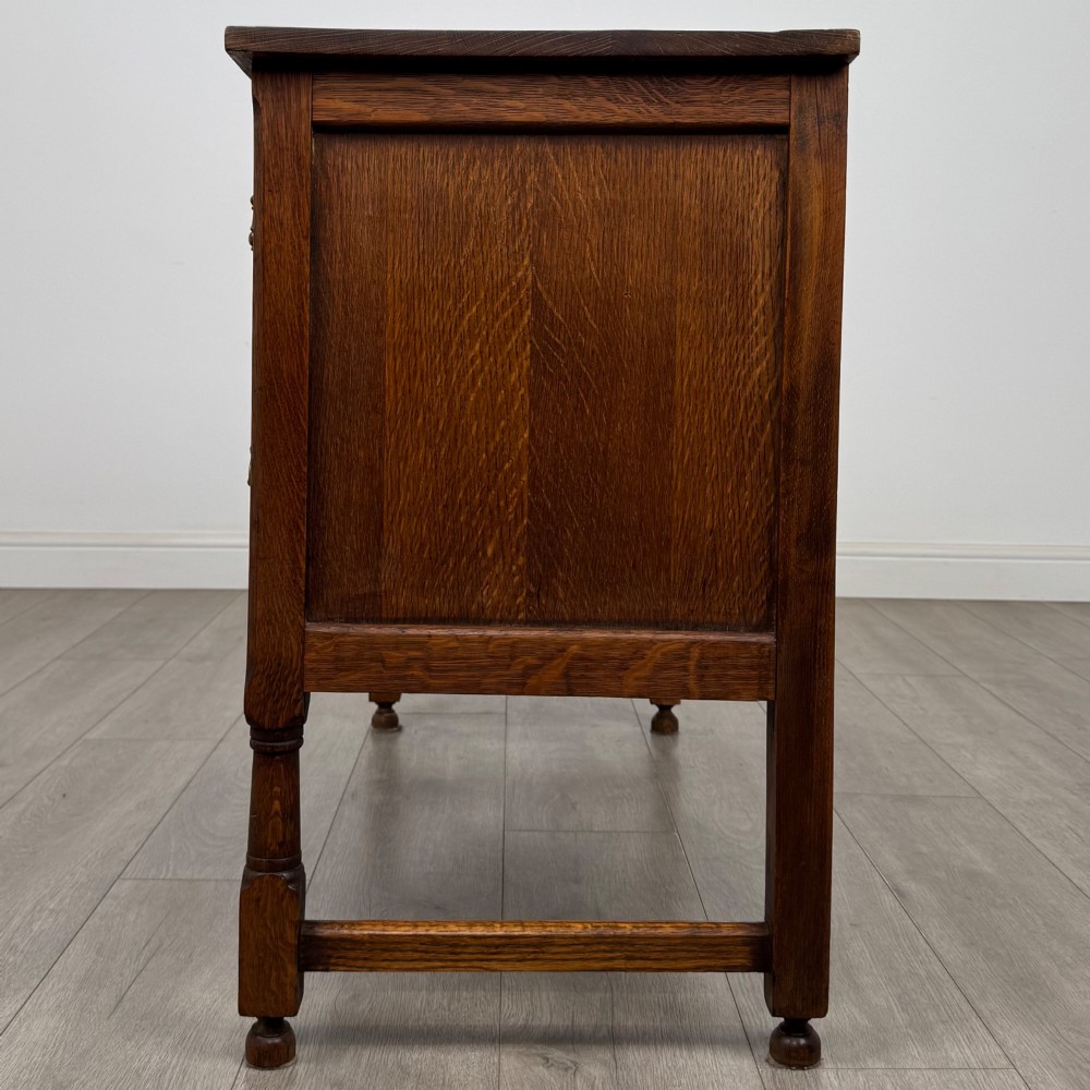 An Edwardian carved oak writing desk featuring five drawers with carved blind arcading, turned legs, stretcher supports, and brass handles. View III