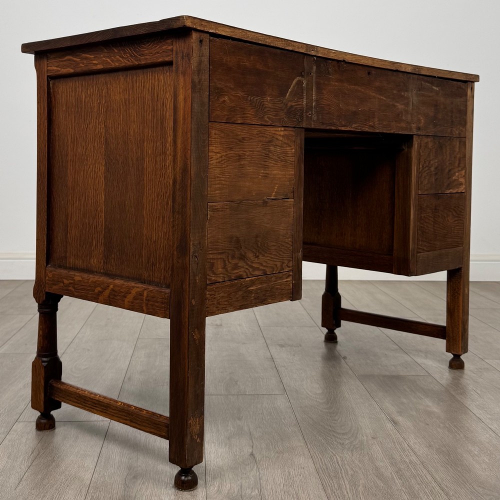 An Edwardian carved oak writing desk featuring five drawers with carved blind arcading, turned legs, stretcher supports, and brass handles. View IV