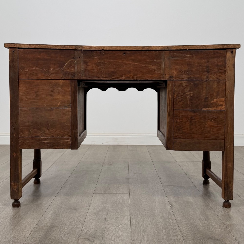 An Edwardian carved oak writing desk featuring five drawers with carved blind arcading, turned legs, stretcher supports, and brass handles. View V