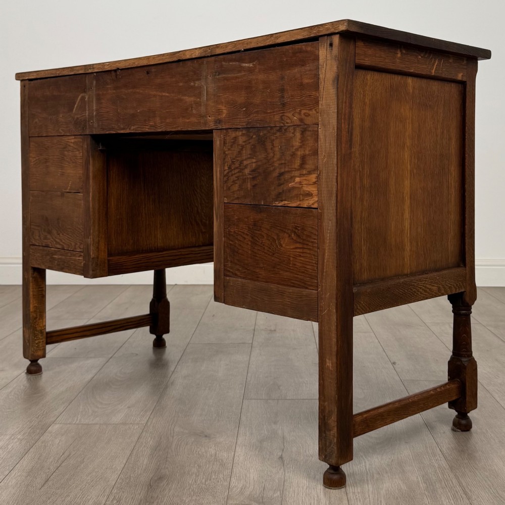 An Edwardian carved oak writing desk featuring five drawers with carved blind arcading, turned legs, stretcher supports, and brass handles. View VI