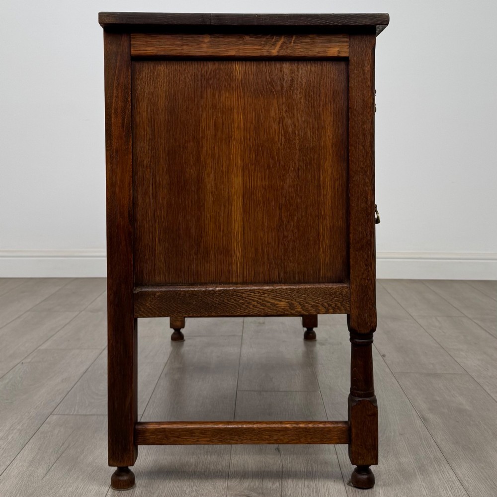An Edwardian carved oak writing desk featuring five drawers with carved blind arcading, turned legs, stretcher supports, and brass handles. View VII