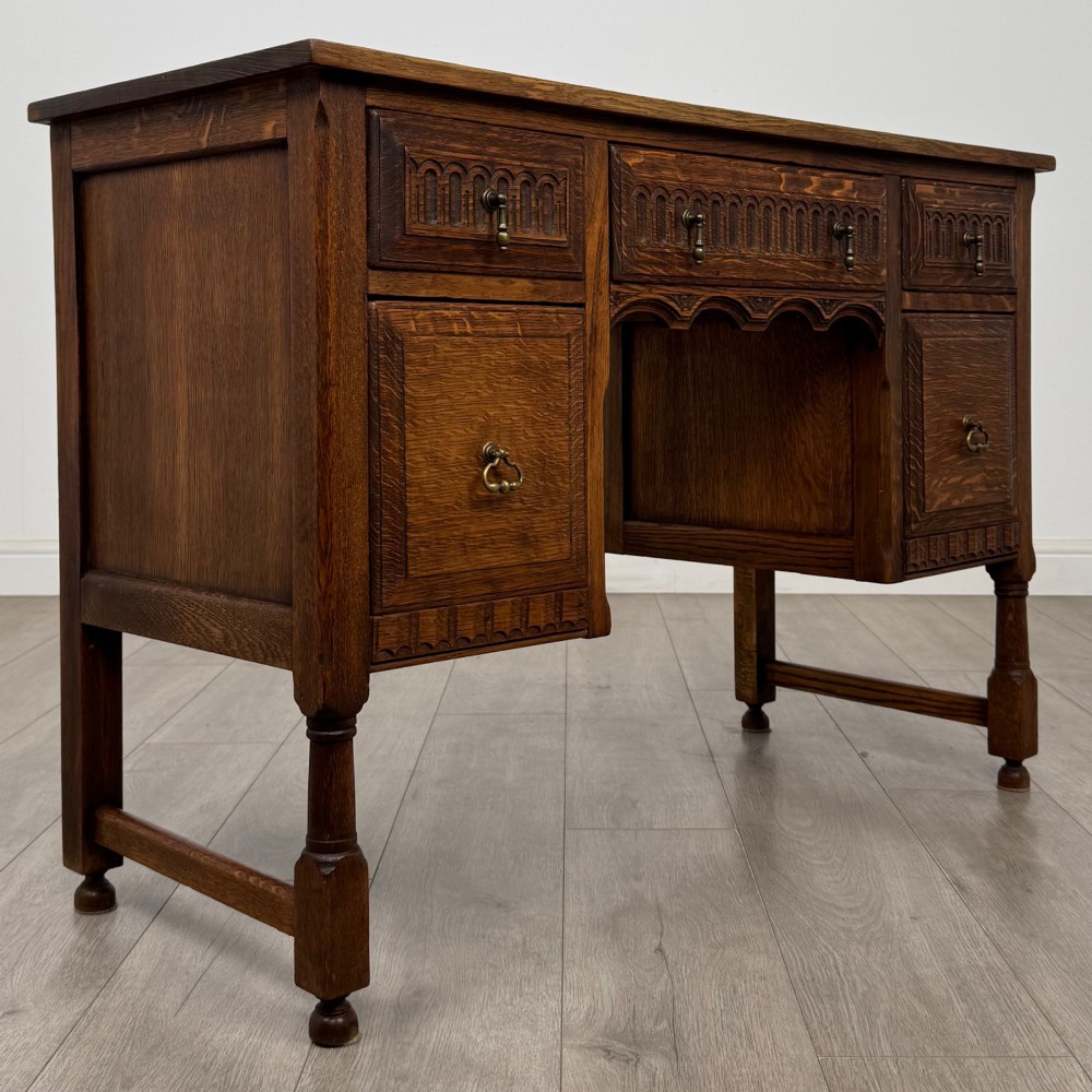 An Edwardian carved oak writing desk featuring five drawers with carved blind arcading, turned legs, stretcher supports, and brass handles. View VIII