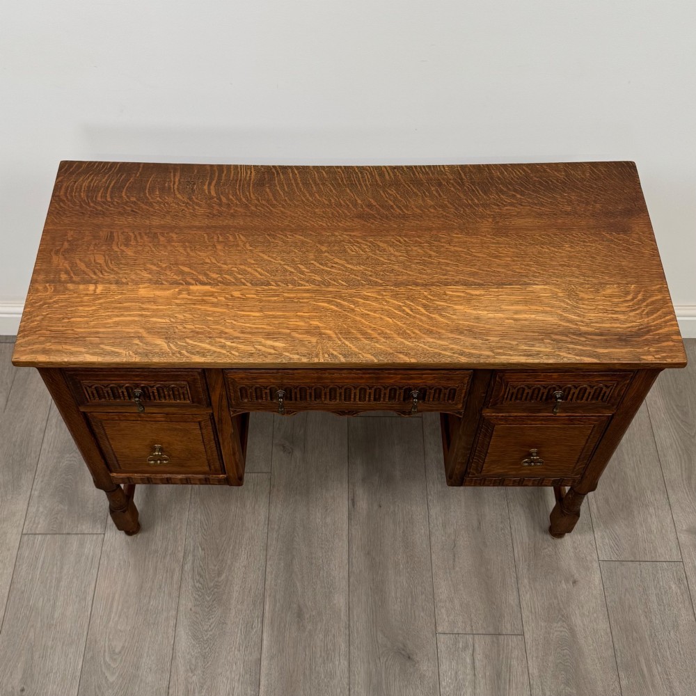 An Edwardian carved oak writing desk featuring five drawers with carved blind arcading, turned legs, stretcher supports, and brass handles. View IX