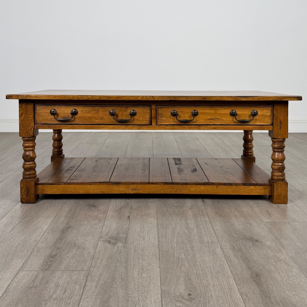 A low rectangular oak coffee table featuring two drawers with metal drop handles, turned legs, and an open lower plank shelf.