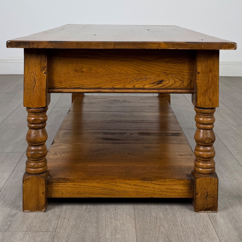 A low rectangular oak coffee table featuring two drawers with metal drop handles, turned legs, and an open lower plank shelf. View III