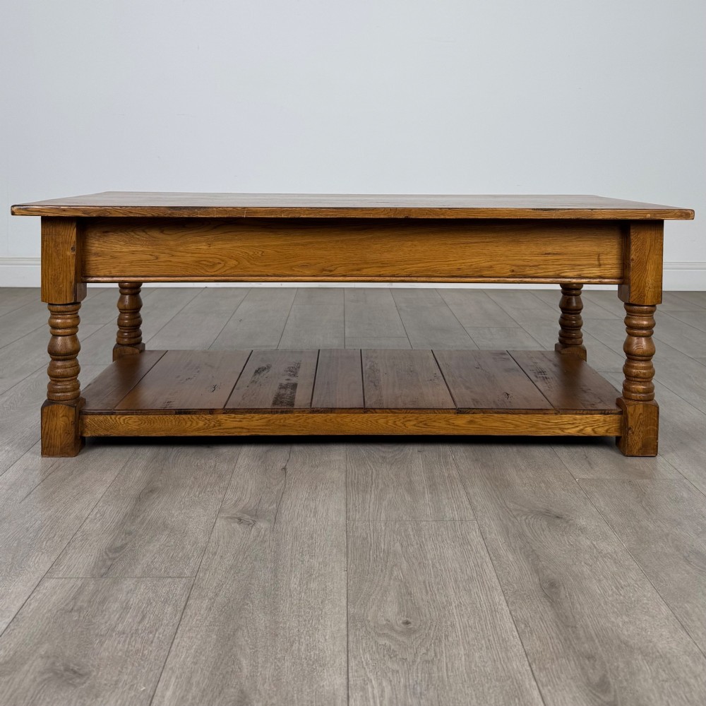 A low rectangular oak coffee table featuring two drawers with metal drop handles, turned legs, and an open lower plank shelf. View V