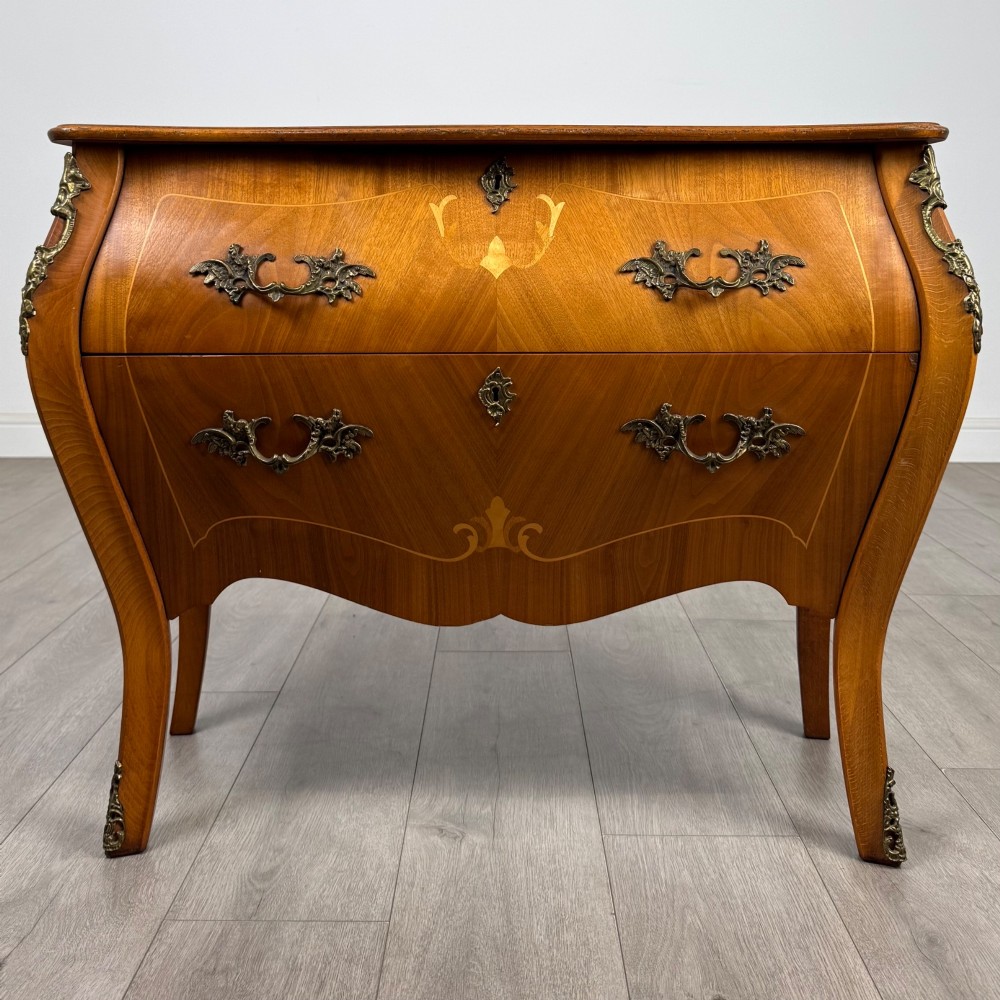 A two-drawer walnut bombe chest featuring curved sides, inlaid marquetry details, cast brass handles, and cabriole legs.