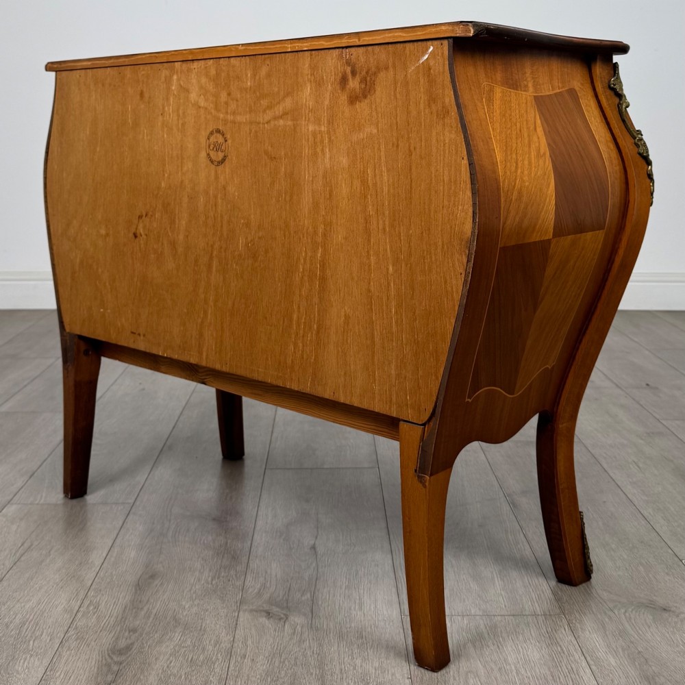 A two-drawer walnut bombe chest featuring curved sides, inlaid marquetry details, cast brass handles, and cabriole legs. View VI