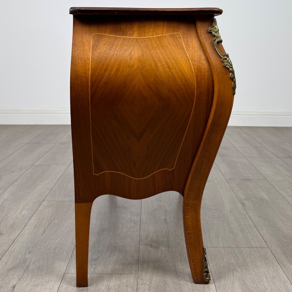 A two-drawer walnut bombe chest featuring curved sides, inlaid marquetry details, cast brass handles, and cabriole legs. View VII