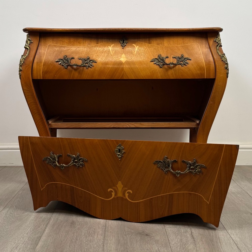 A two-drawer walnut bombe chest featuring curved sides, inlaid marquetry details, cast brass handles, and cabriole legs. View X