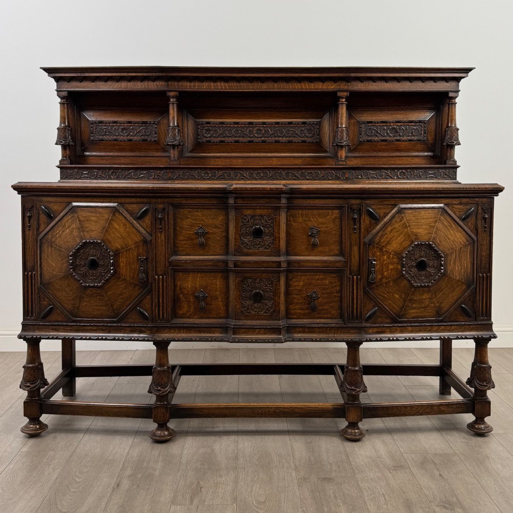 A large 19th-century dark carved oak sideboard featuring a raised upper gallery with carved panels, geometric cupboard doors, central drawers, and turned legs joined by stretchers.