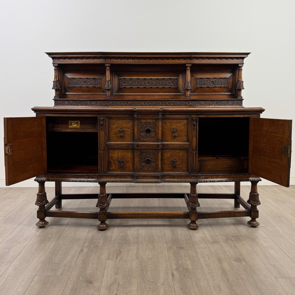 A large 19th-century dark carved oak sideboard featuring a raised upper gallery with carved panels, geometric cupboard doors, central drawers, and turned legs joined by stretchers. View II
