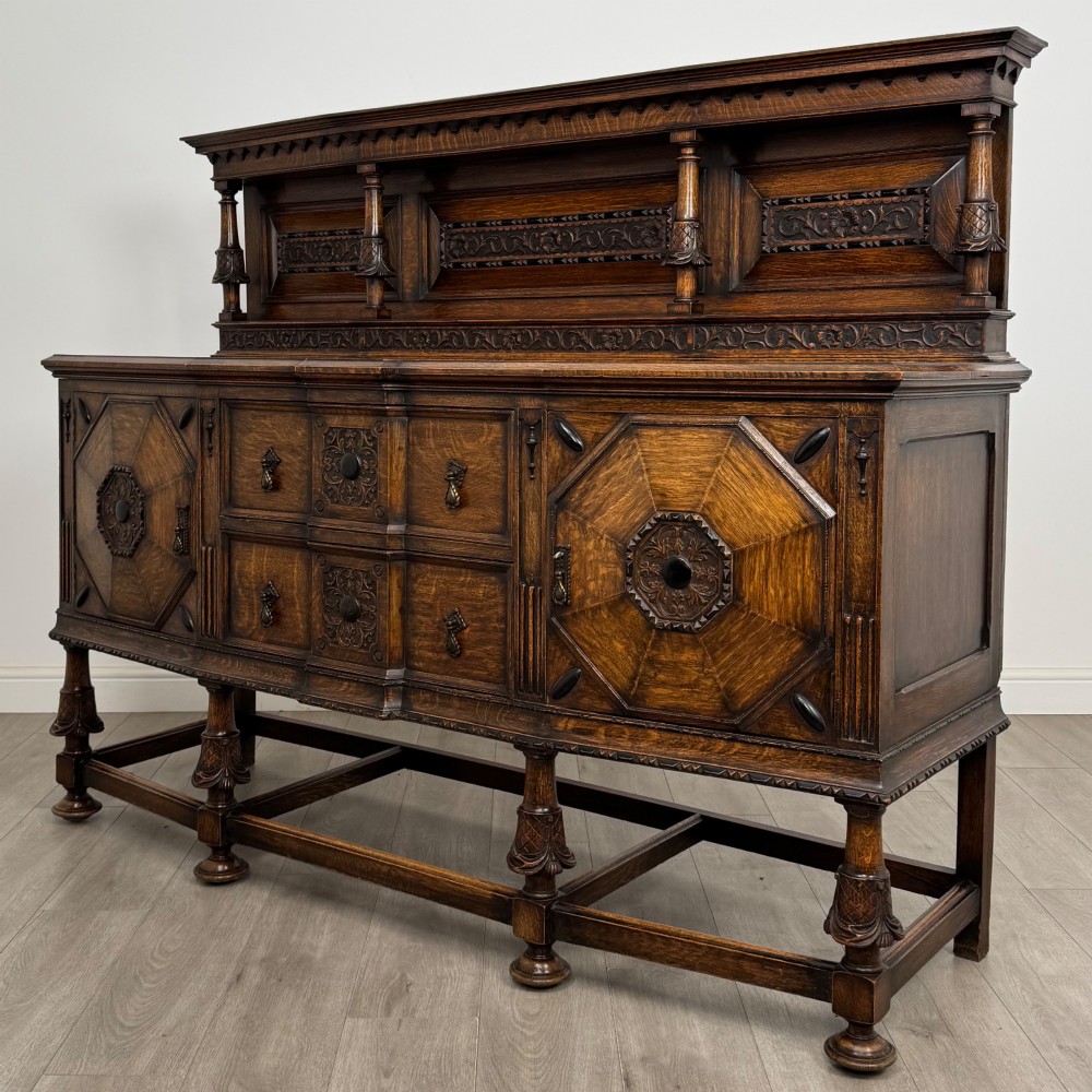 A large 19th-century dark carved oak sideboard featuring a raised upper gallery with carved panels, geometric cupboard doors, central drawers, and turned legs joined by stretchers. View III