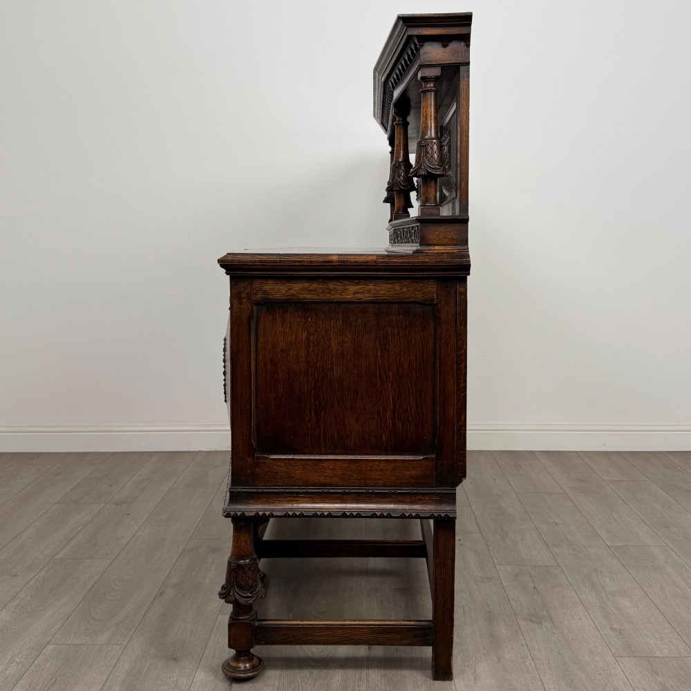 A large 19th-century dark carved oak sideboard featuring a raised upper gallery with carved panels, geometric cupboard doors, central drawers, and turned legs joined by stretchers. View IV