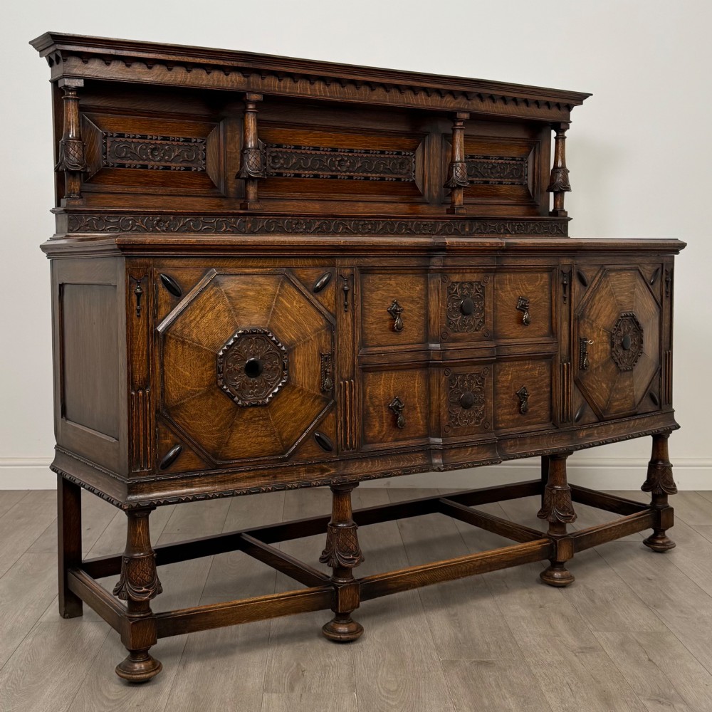 A large 19th-century dark carved oak sideboard featuring a raised upper gallery with carved panels, geometric cupboard doors, central drawers, and turned legs joined by stretchers. View IX