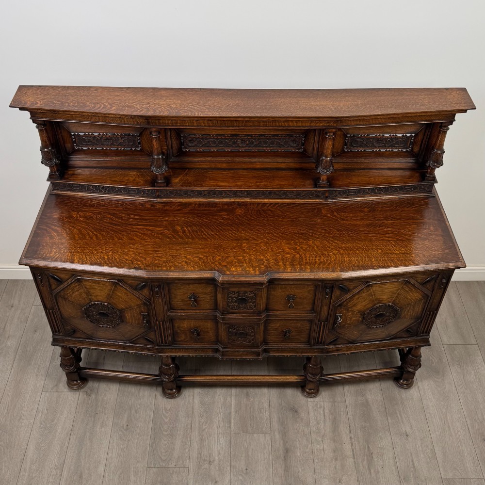 A large 19th-century dark carved oak sideboard featuring a raised upper gallery with carved panels, geometric cupboard doors, central drawers, and turned legs joined by stretchers. View X