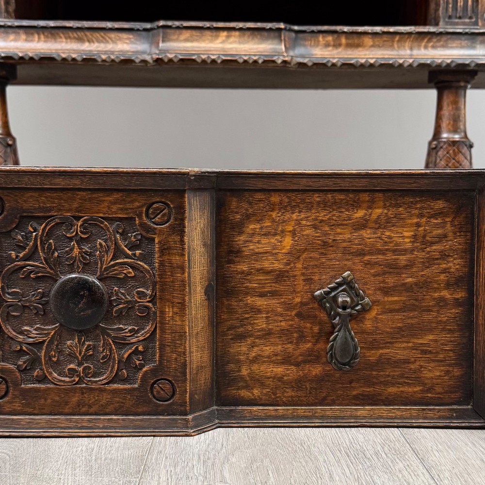 A large 19th-century dark carved oak sideboard featuring a raised upper gallery with carved panels, geometric cupboard doors, central drawers, and turned legs joined by stretchers. View XII