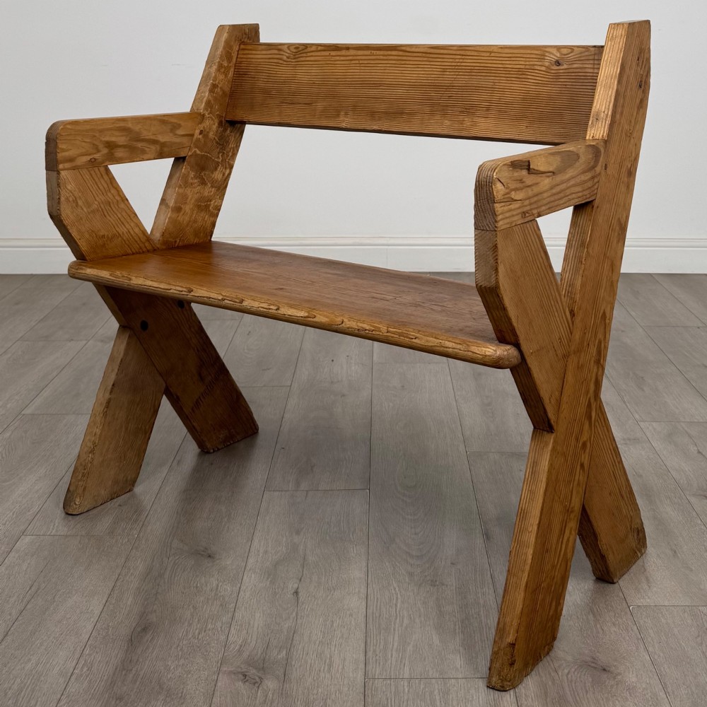 A nineteenth-century pitch pine bench featuring an X-frame structure, integrated side armrests, and a single horizontal back rail.