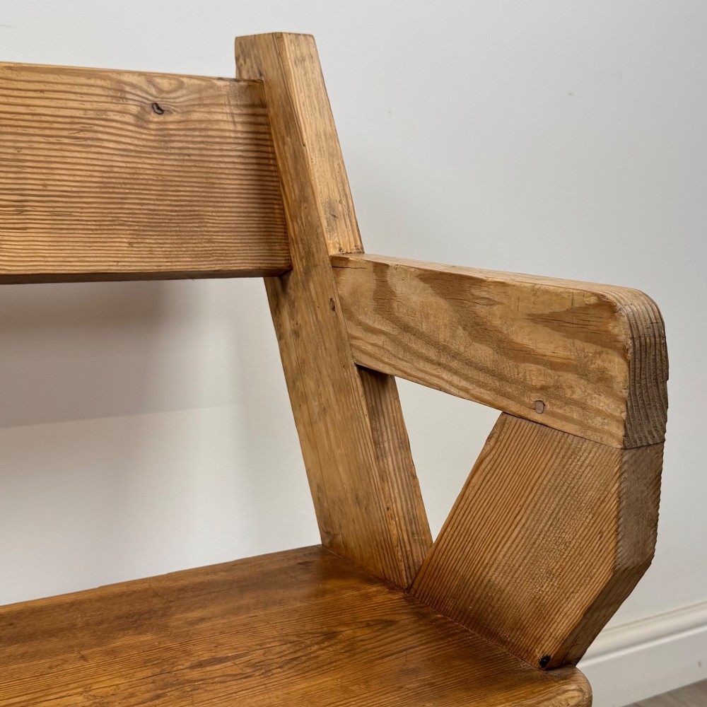 A nineteenth-century pitch pine bench featuring an X-frame structure, integrated side armrests, and a single horizontal back rail. View X