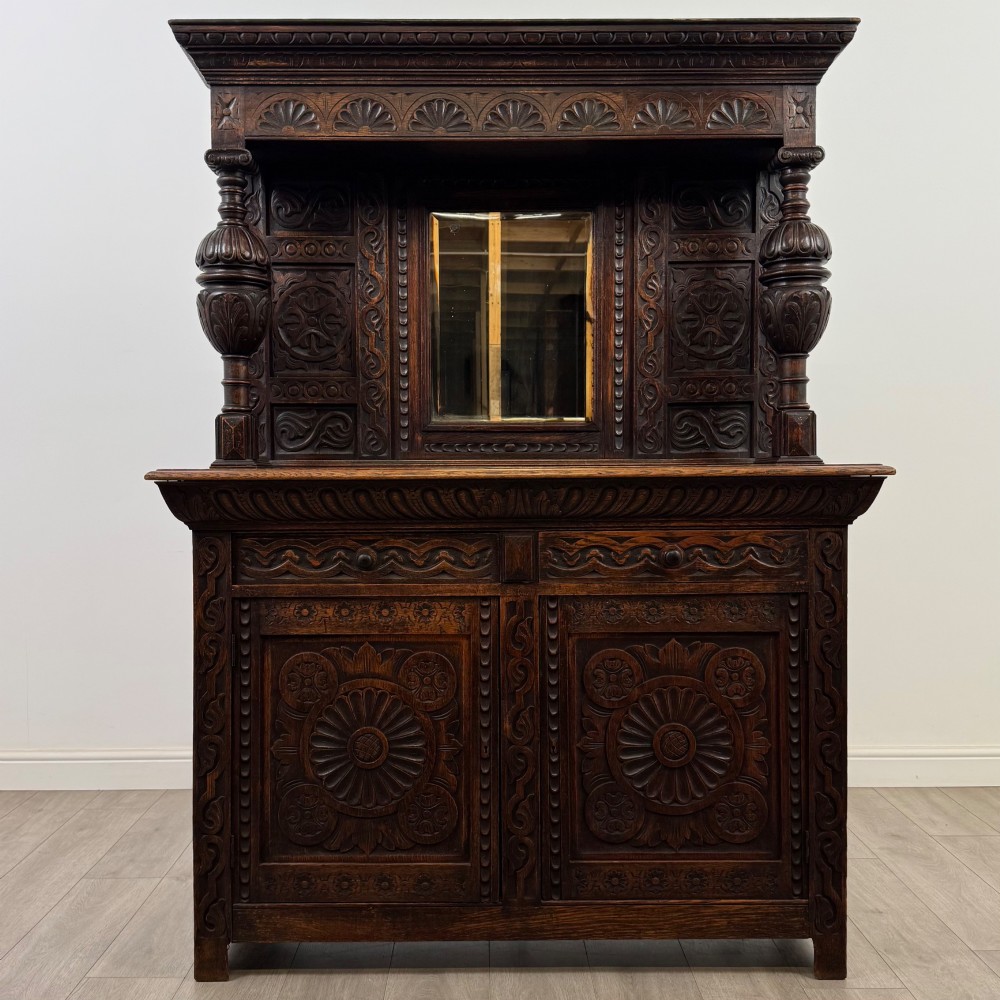 A 19th-century dark carved oak Victorian sideboard featuring an upper mirrored shelf section supported by turned bulbous pilasters above two carved drawers and cupboard doors with rosette reliefs.