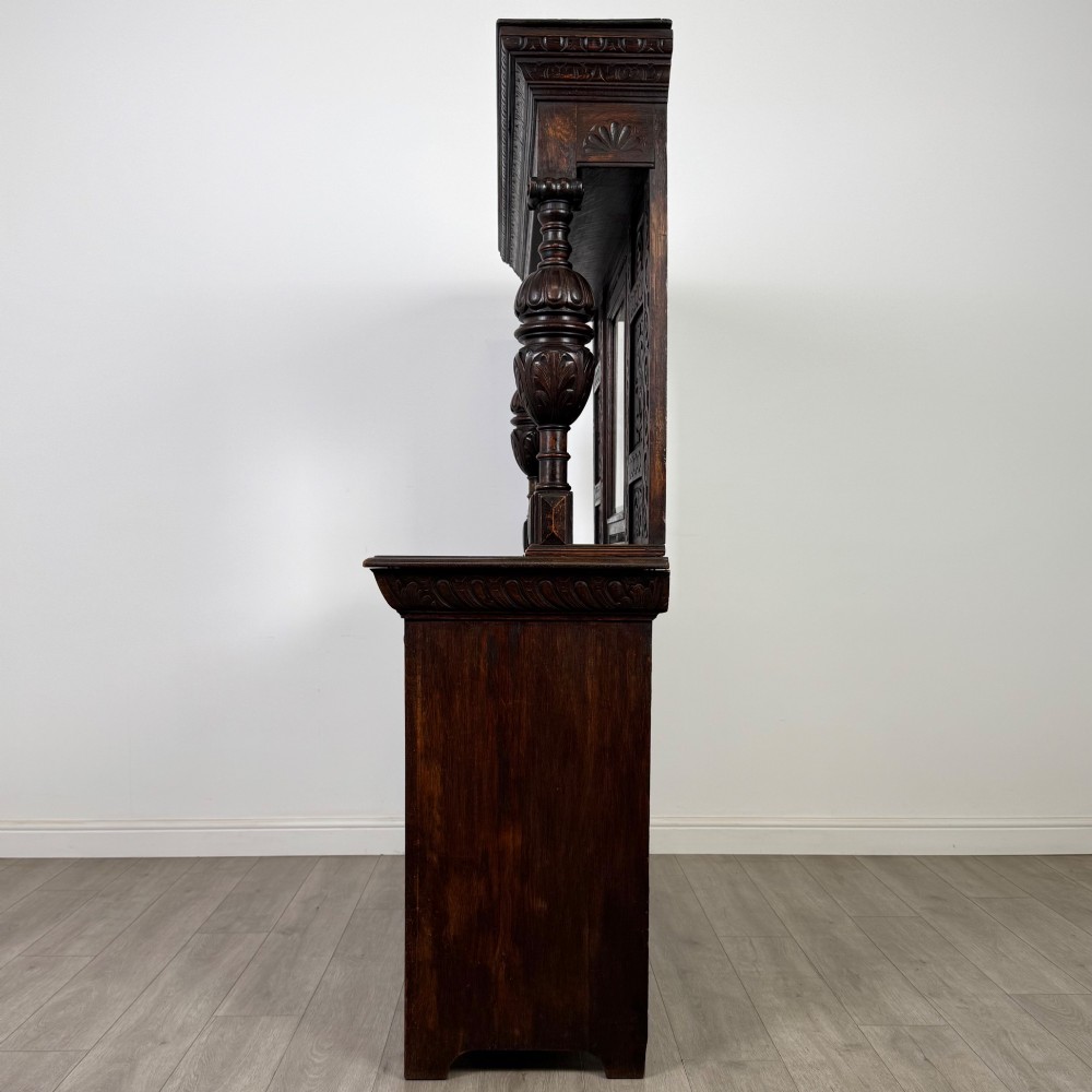 A 19th-century dark carved oak Victorian sideboard featuring an upper mirrored shelf section supported by turned bulbous pilasters above two carved drawers and cupboard doors with rosette reliefs. View IV